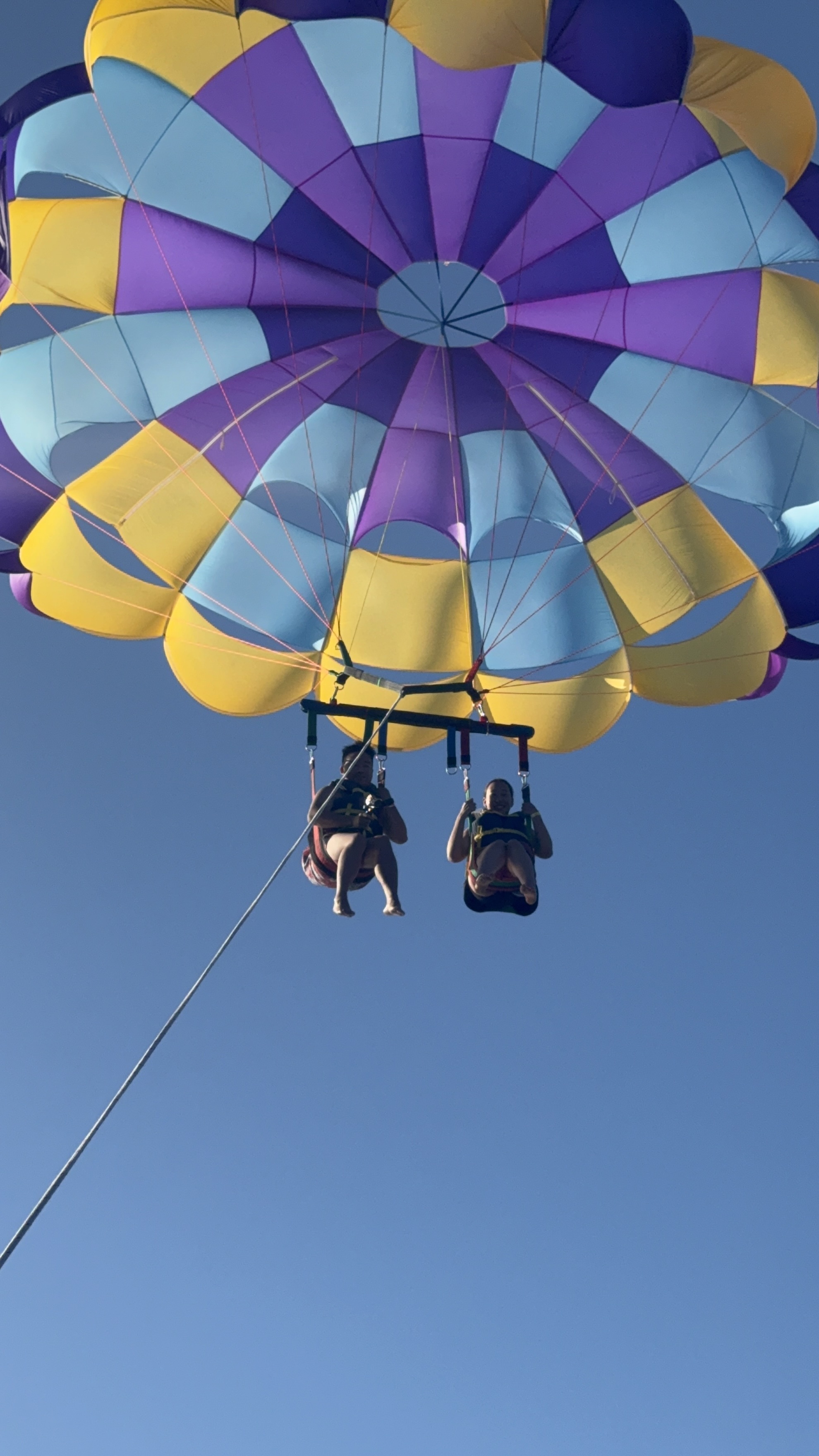 Two people parasailing with a colorful parachute against a clear blue sky