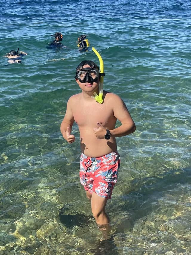 A person wearing a snorkel and mask is walking out of the water, with others snorkeling in the background
