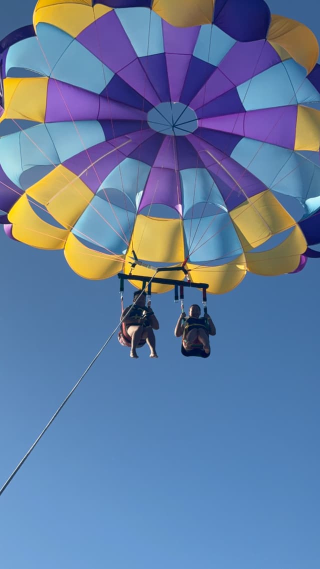 Two people parasailing with a colorful parachute against a clear blue sky